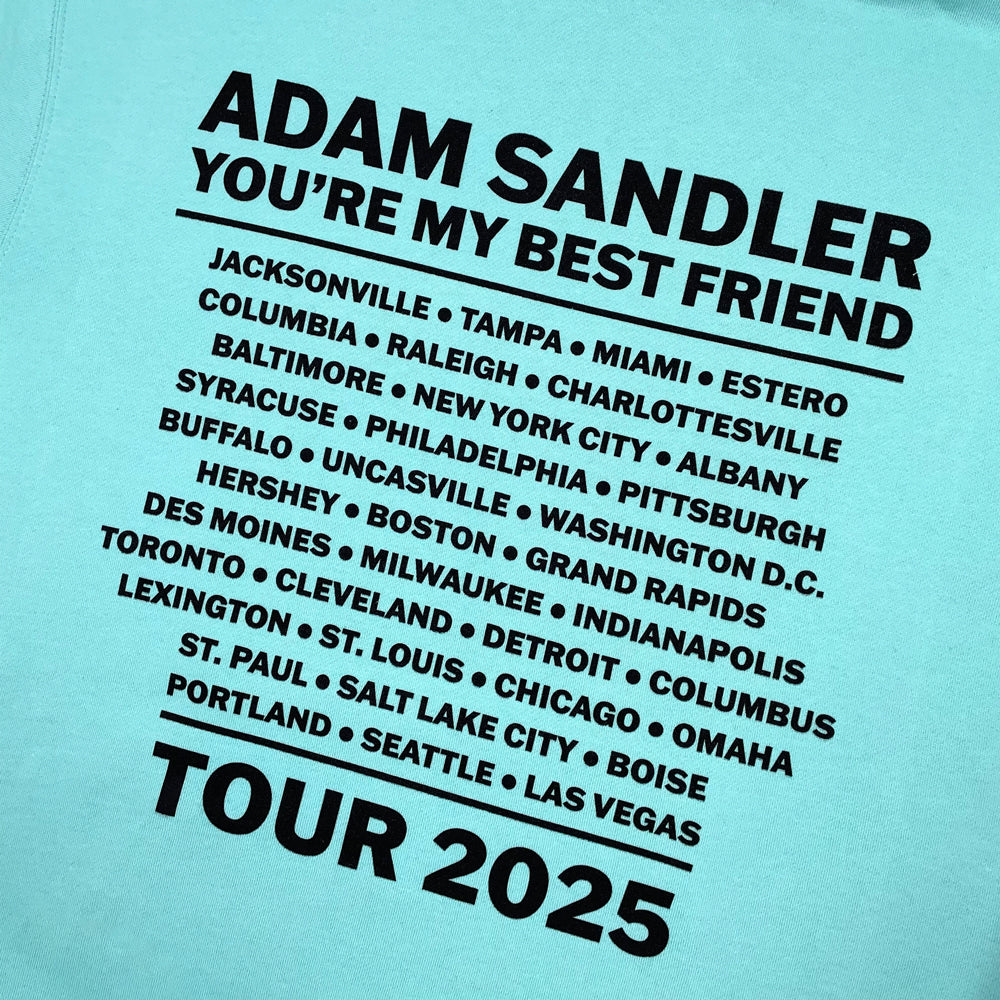Close up of a mint colored hoodie with black text providing list of cities and information from the Adam Sandler "You're my Best Friend Tour" on the back