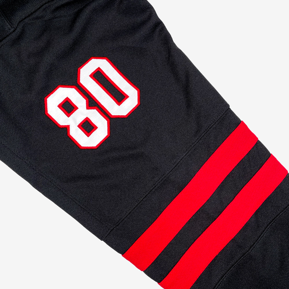 Close up of a hockey jersey sleeve with two red stripes and with white with a red out line of the number "80" against a white background.