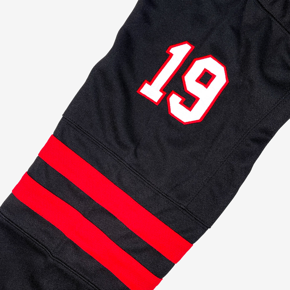 Close up of a hockey jersey sleeve with two red stripes and with white with a red out line of the number "19" against a white background.