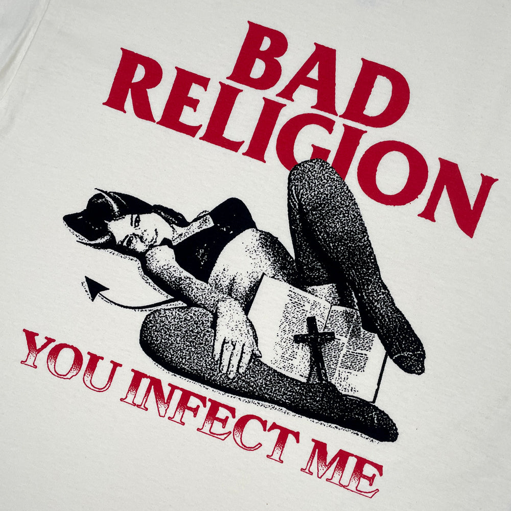 Cream t-shirt with graphic of a woman and cross with red text reading "BAD RELIGION YOU INFECT ME" against a white background