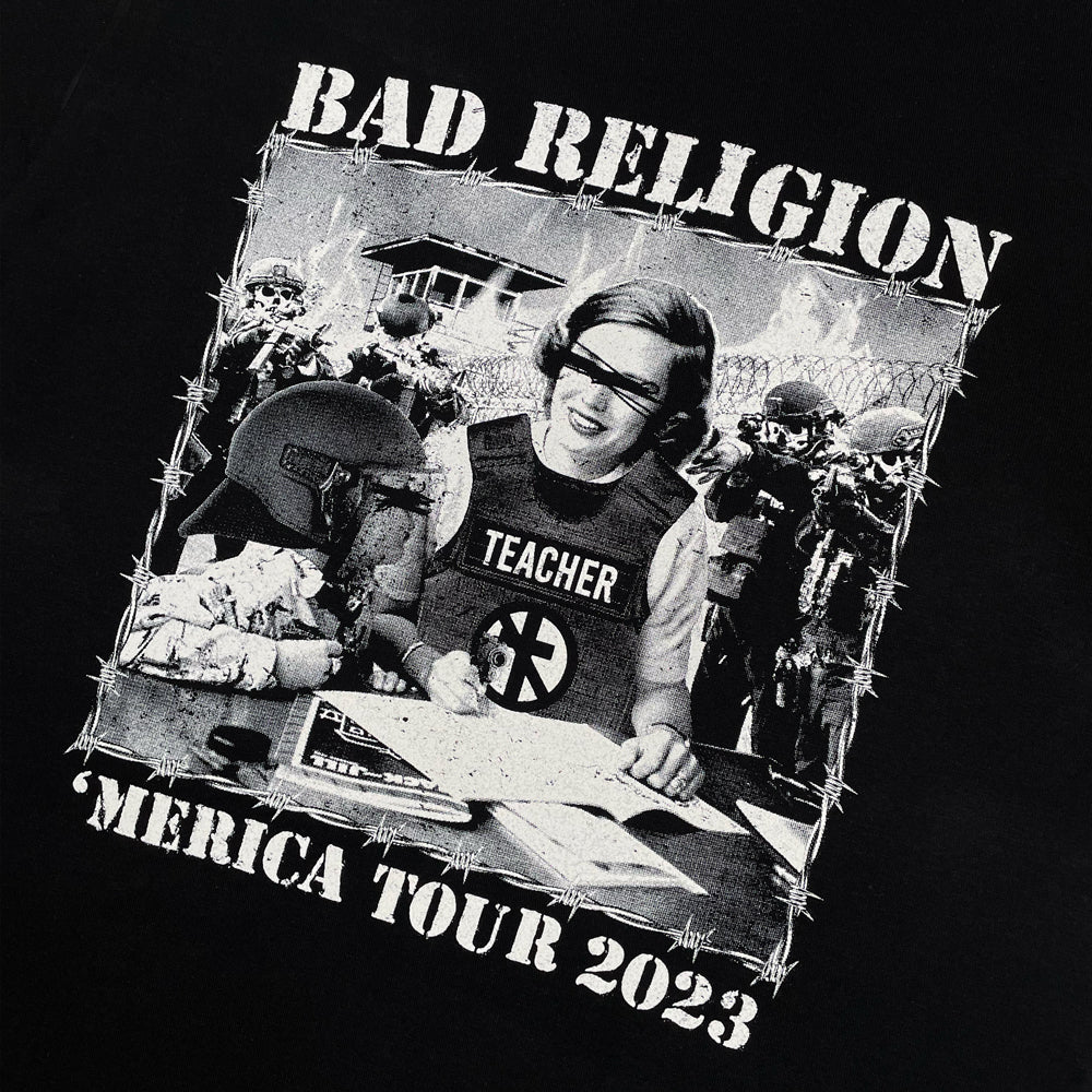 Close up of a front print of black Bad Religion t-shirt with graphic of a teacher surrounded by men pointing a gun at them. Graphic is surrounded by lettering reading "Bad Religion 'Merica Tour 2023"
