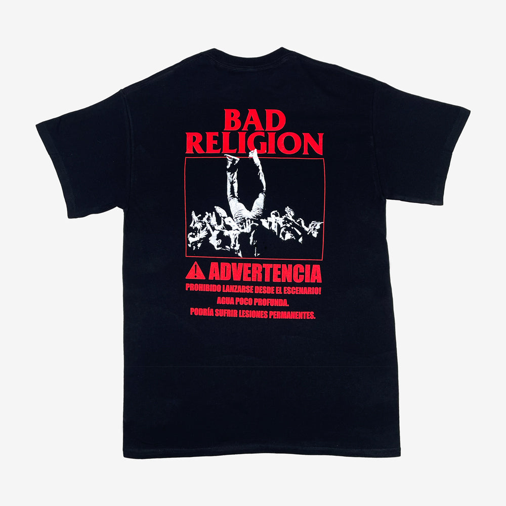Back of a black tee against a white background with red text reading "Bad Religion, Advertencia, Prohibido Lanzarse Desde El Escenario! Agua Poco Profunda, Podría Sufrir Lesones Permanentes." With a white graphic of a person crowd surfing.