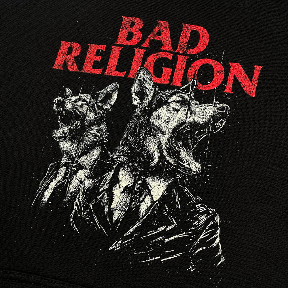 Close up of the front of a black pullover hoodie against a white background featuring a design of two dogs wearing suits printed in light gray ink. Above the dogs in red text it reads Bad Religion." 