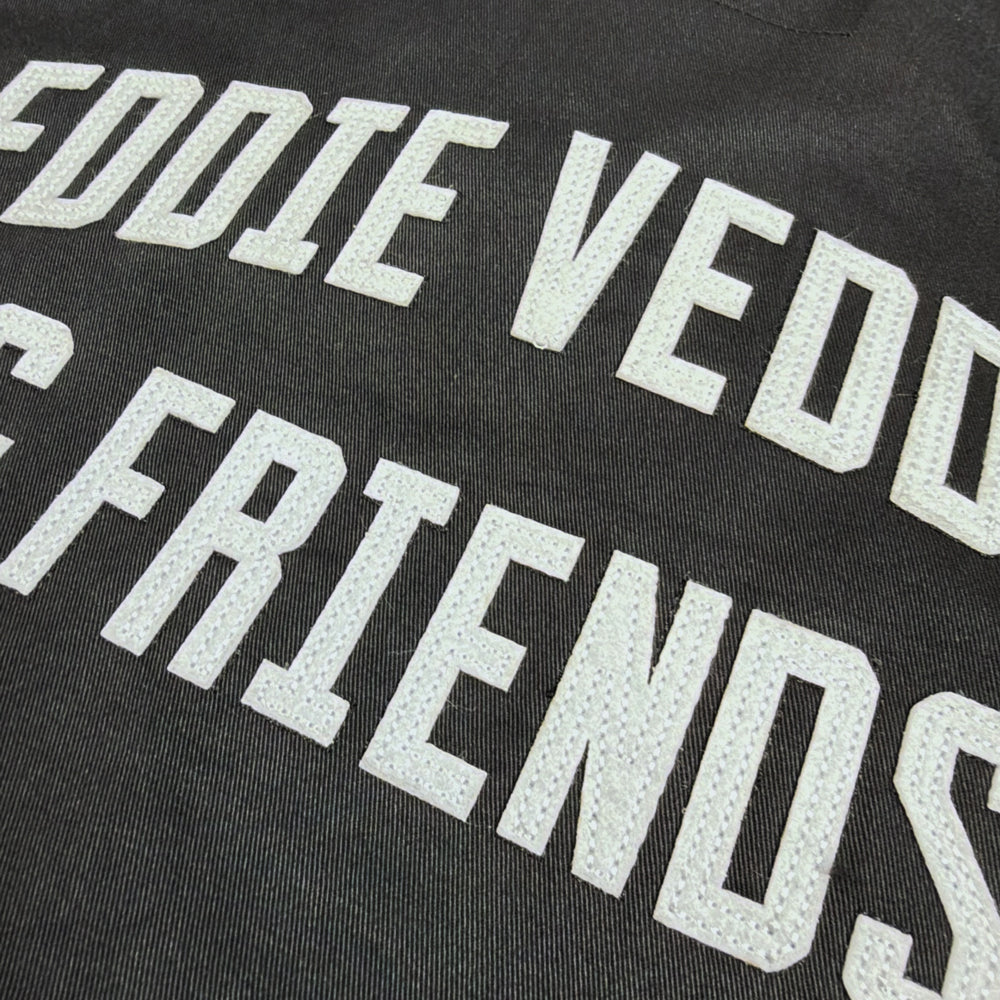 Close-up of textured white Eddie Vedder & Friends appliqué lettering and stitching on black jacket