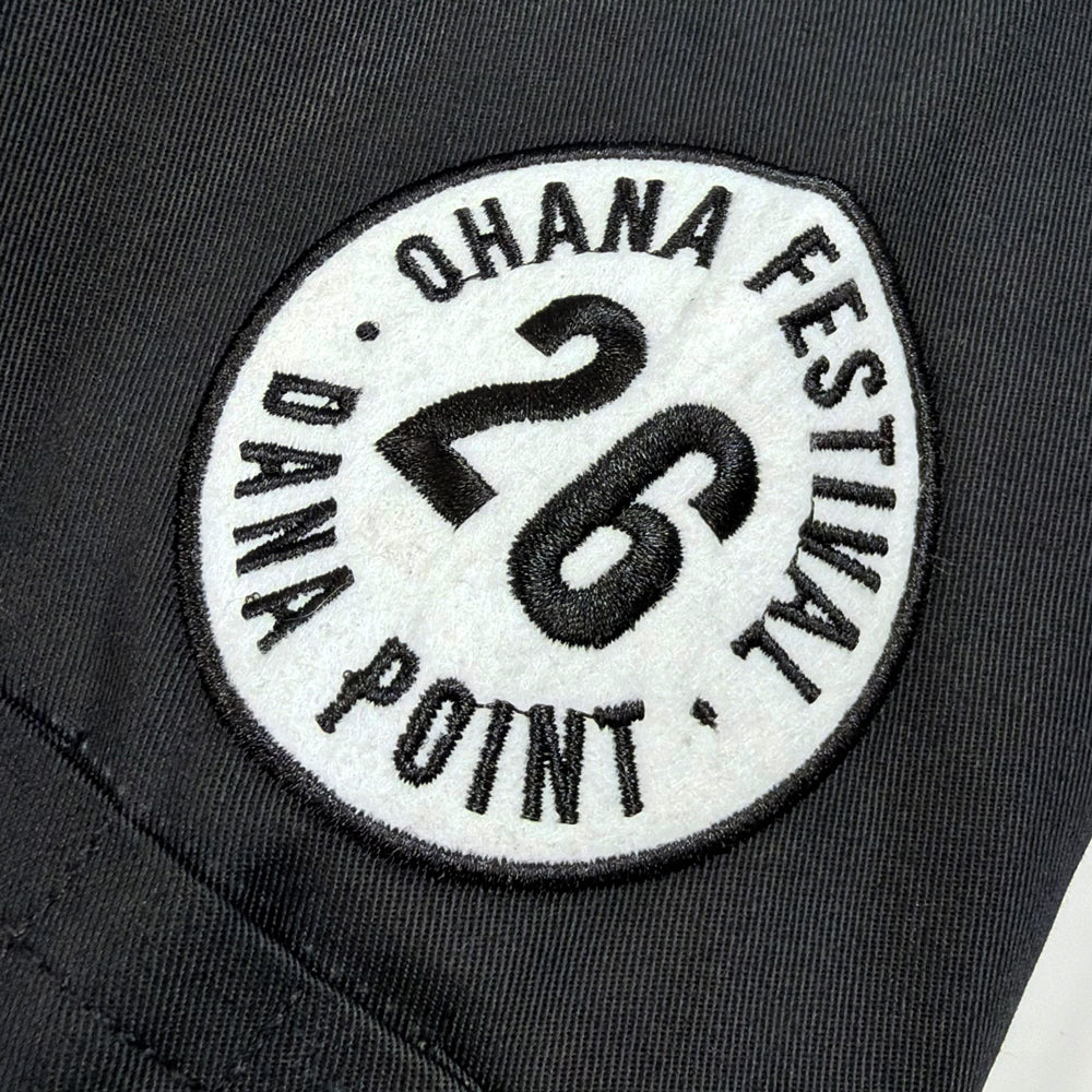 Close-up of circular white patch embroidered with Ohana Festival, Dana Point, and 26 on black jacket sleeve