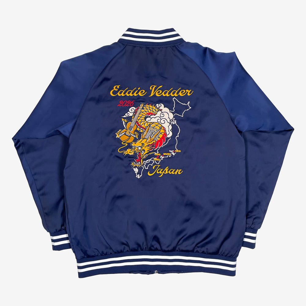 The back of a navy jacket with white stripes on the collar, cuff, and hip against a white background. Centered on the back is a yellow, orange, and red dragon holding a guitar. the dragon is flying in the clouds and behind the dragon is a white outline of Japan. In yellow the names of the cities of the tour are highlighted. In yellow text on top reads "Eddie Vedder" and below there is yellow text that reads "Japan"