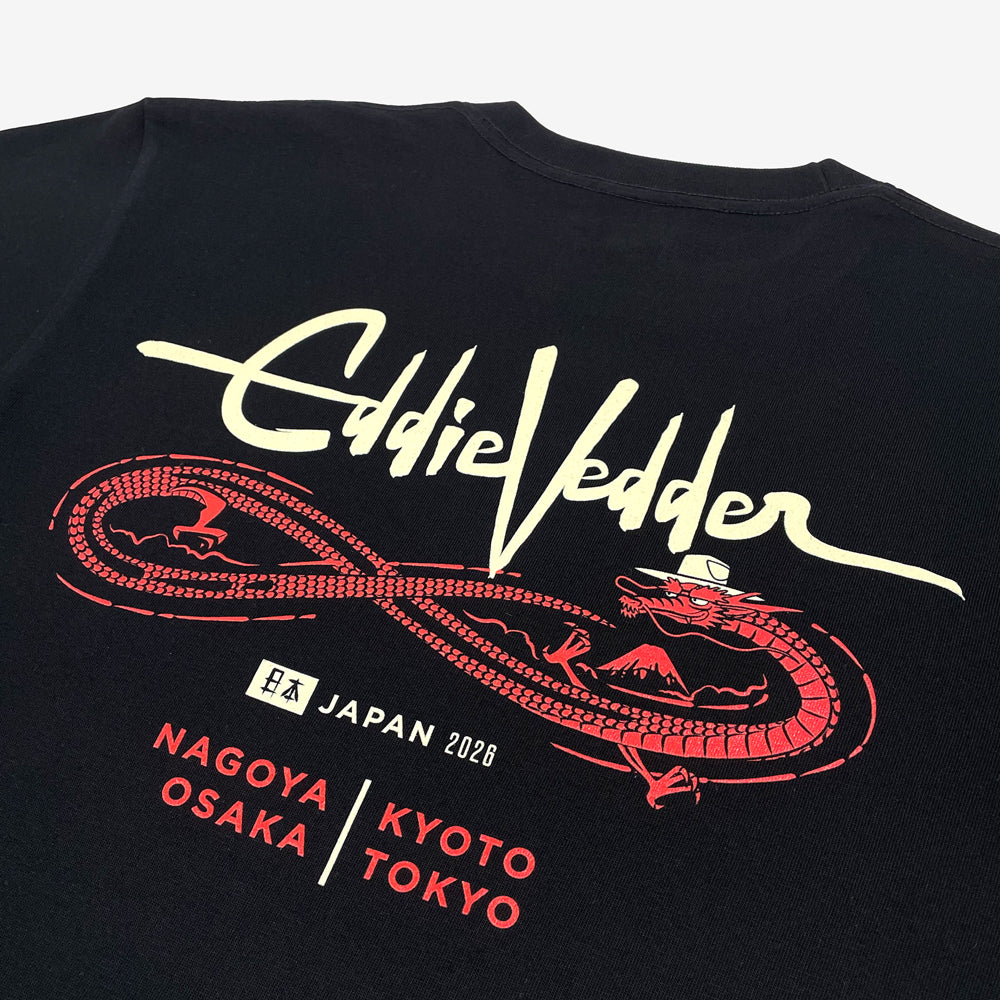 Close up of the back of a black T shirt against a white background with a light beige text design reading "Eddie Vedder" with a red design of a dragon below. Below the dragon there is light beige text reading "Japan 2026" followed by "Nagoya, Osaka, Kyoto, Tokyo" in red text"