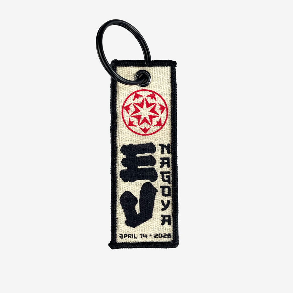 A flight tag keychain against a white background. At the top of the flight tag is a red circular design. In the middle is large black text reading "EV" and to the right of that is black text reading "Nagoya" At the bottom in black text there is a date that reads "April 14, 2026"
