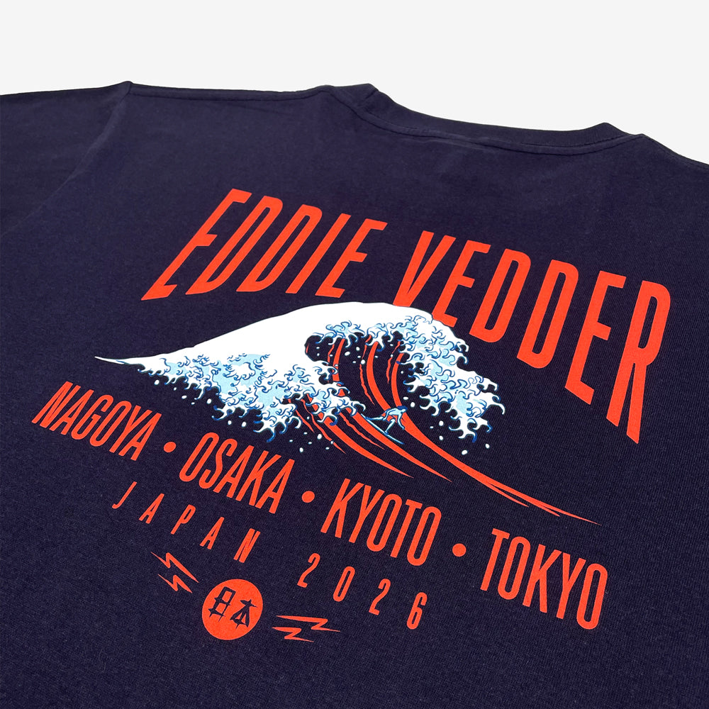 Close up of the back of a navy T shirt against a white background with red text reading "Eddie Vedder." Below that is a design of a great wave. Below the wave is more red text reading "Nagoya, Osaka, Kyoto, Tokyo, Japan 2026"