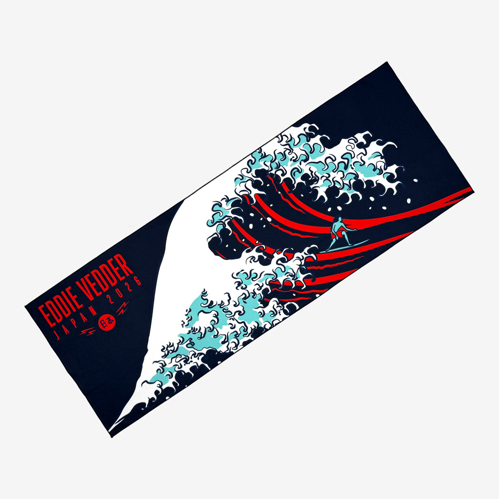 A Tenugui towel against a white background. There is a design featuring a great wave and a person surfing it. On the top left corner in red text there is lettering that reads, "Eddie Vedder Japan 2026"