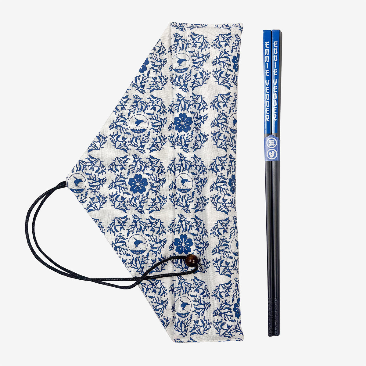 A pair of chopsticks and a white cloth bag against a white background. The chopsticks are black with blue ends with white text reading "Eddie Vedder." The cloth bag has a blue floral pattern on it as well as a pattern of a circular design showing a man balancing on top of Mt. Fuji.