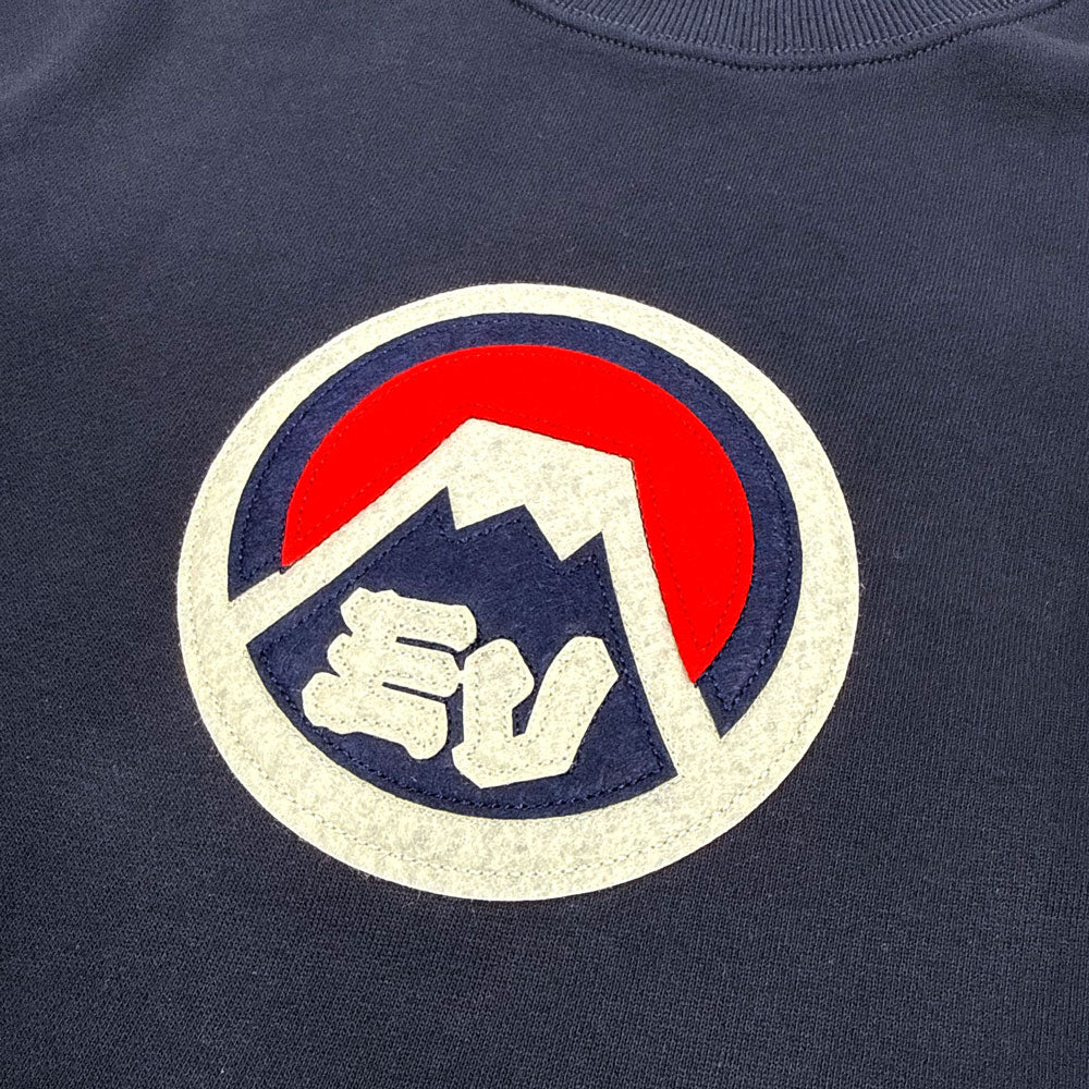 Navy blue crewneck sweatshirt with a circular logo featuring a white circle with a mountain design and the initials "EV"