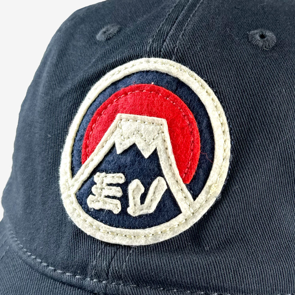 Navy blue cap with a circular patch featuring a mountain design and "EV" initials on a white background
