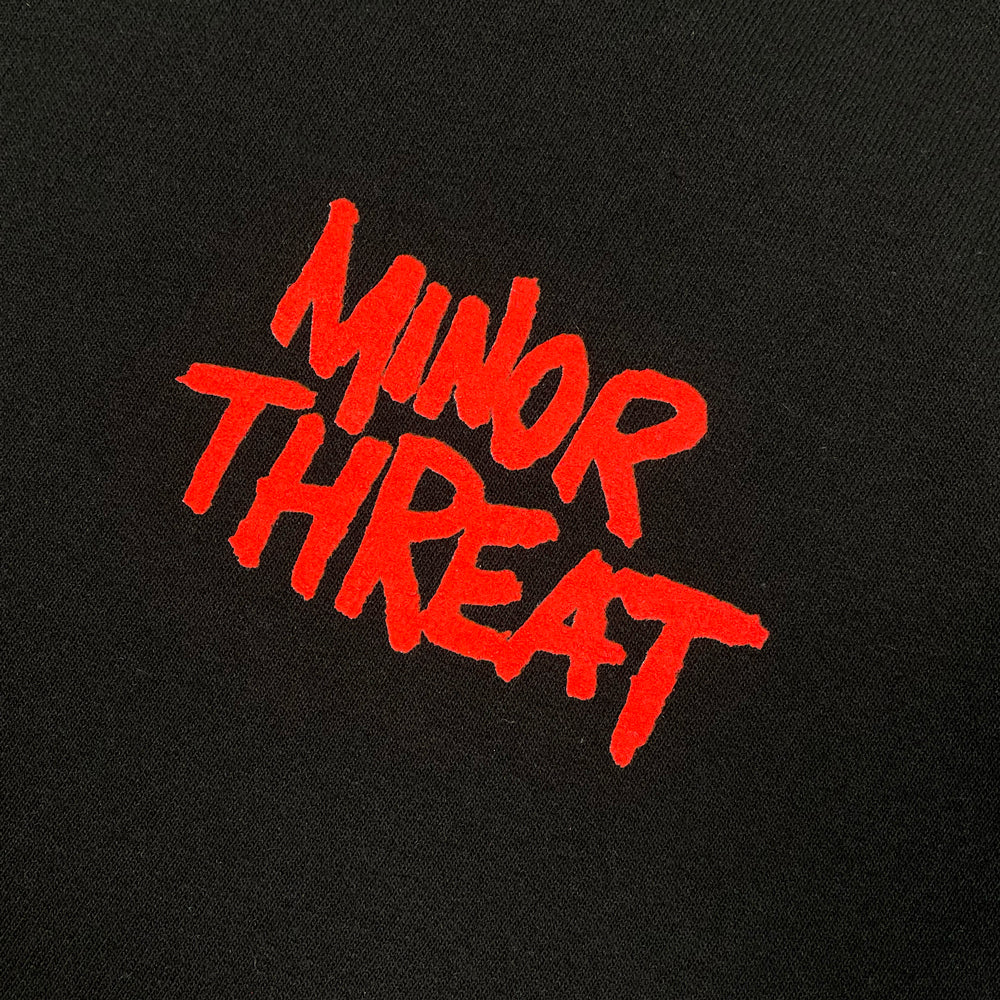 Close up of a black sweatshirt with red typography on left chest reading "Minor Threat"
