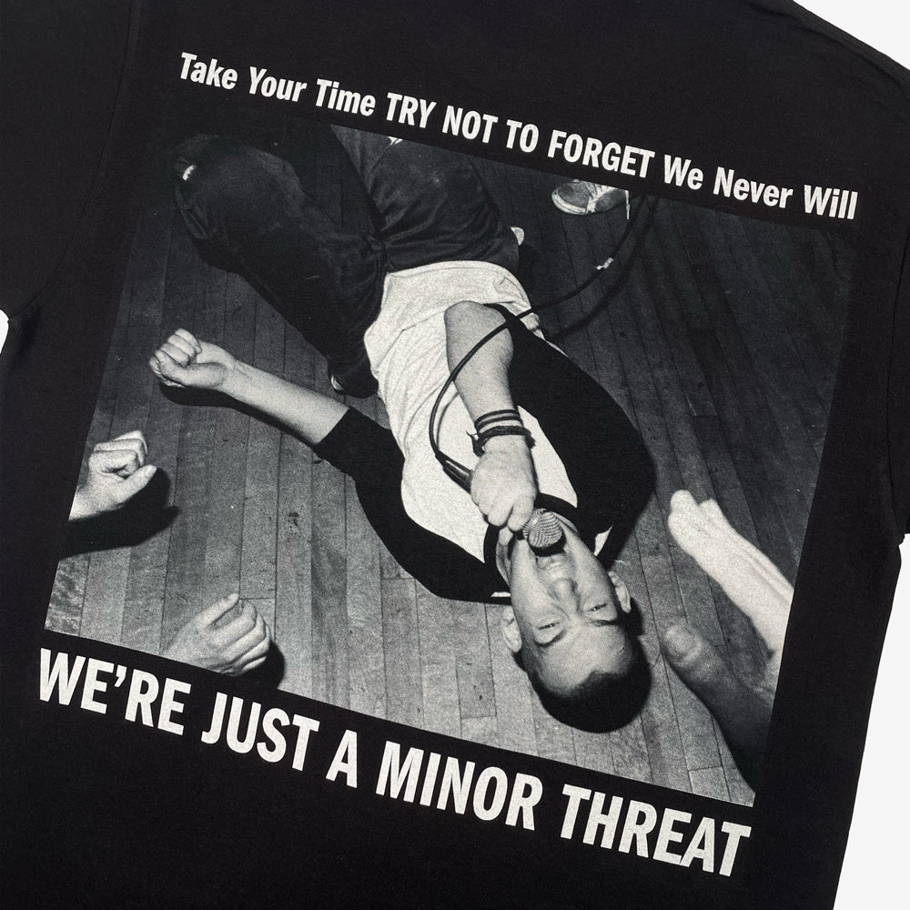 Close up of the back of a Minor Threat black tee featuring image of Minor Threat performing surrounded by the words "Take Your Time TRY NOT TO FORGET We Never Will WE'RE JUST A MINOR THREAT"