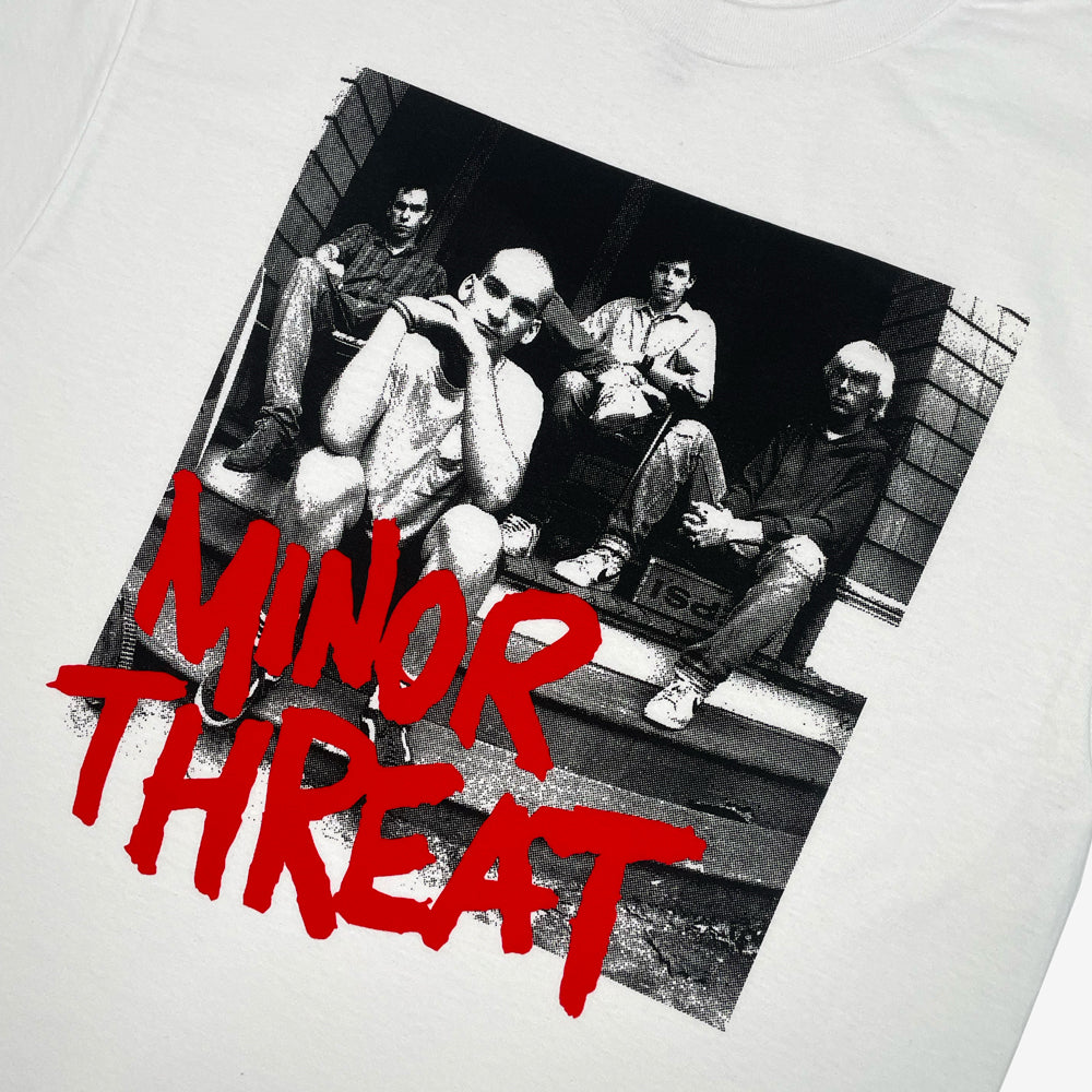 Close up of a white T shirt on a white background with a black and white photo of the four members of Minor Threat sitting on a porch behind red text reading "Minor Threat"