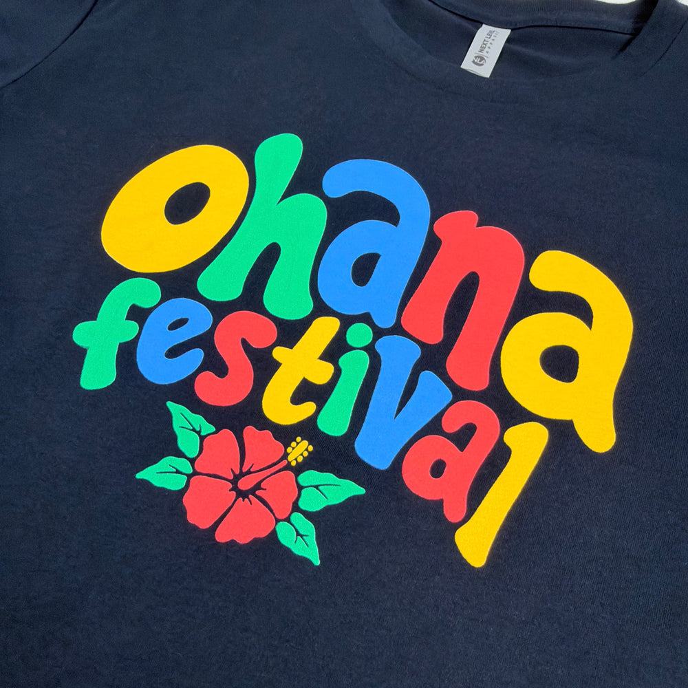Close-up of colorful Ohana Festival bubble lettering and a pink hibiscus with green leaves on navy fabric.