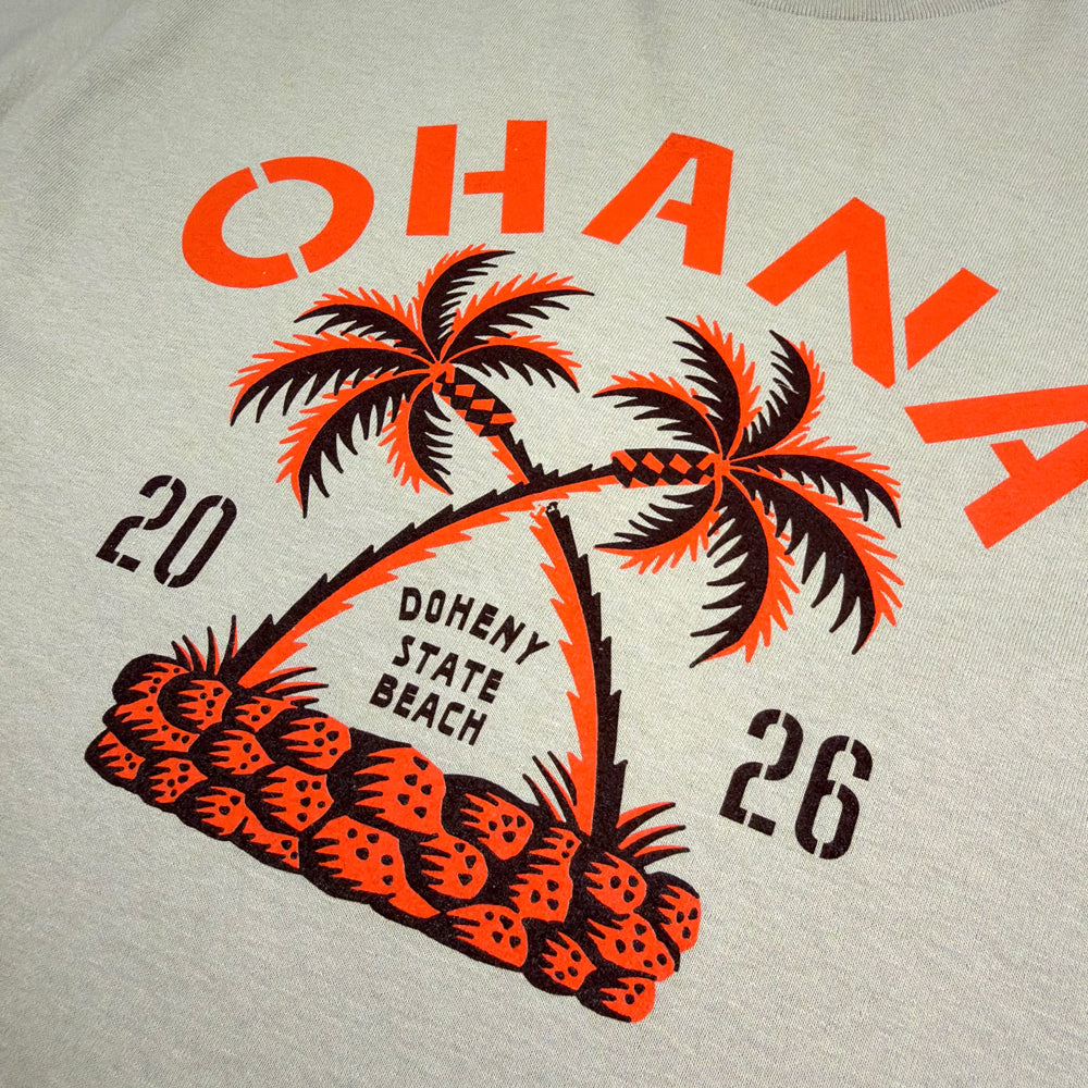 Close-up of crossed palm trees and Doheny State Beach lettering on the sand Ohana Crossed Palms Tee.