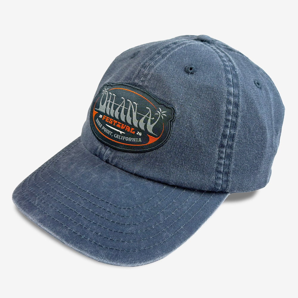 Three-quarter view of the washed navy Ohana Drop In Hat showing its festival patch and curved brim.