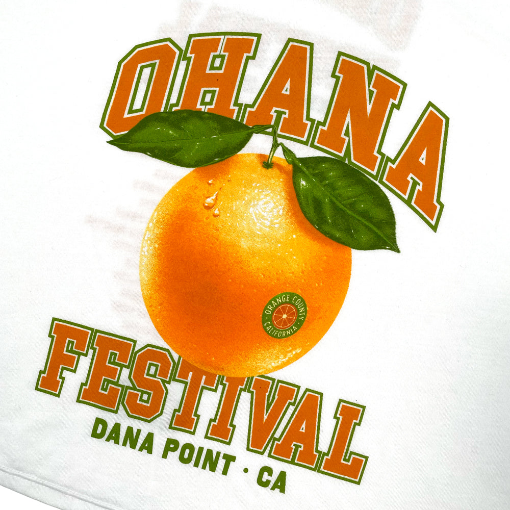 A close up of a white Ohana Festival t-shirt from the front with graphic of an orange surrounded by lettering reading "Ohana Festival Dana Point, CA" against white background