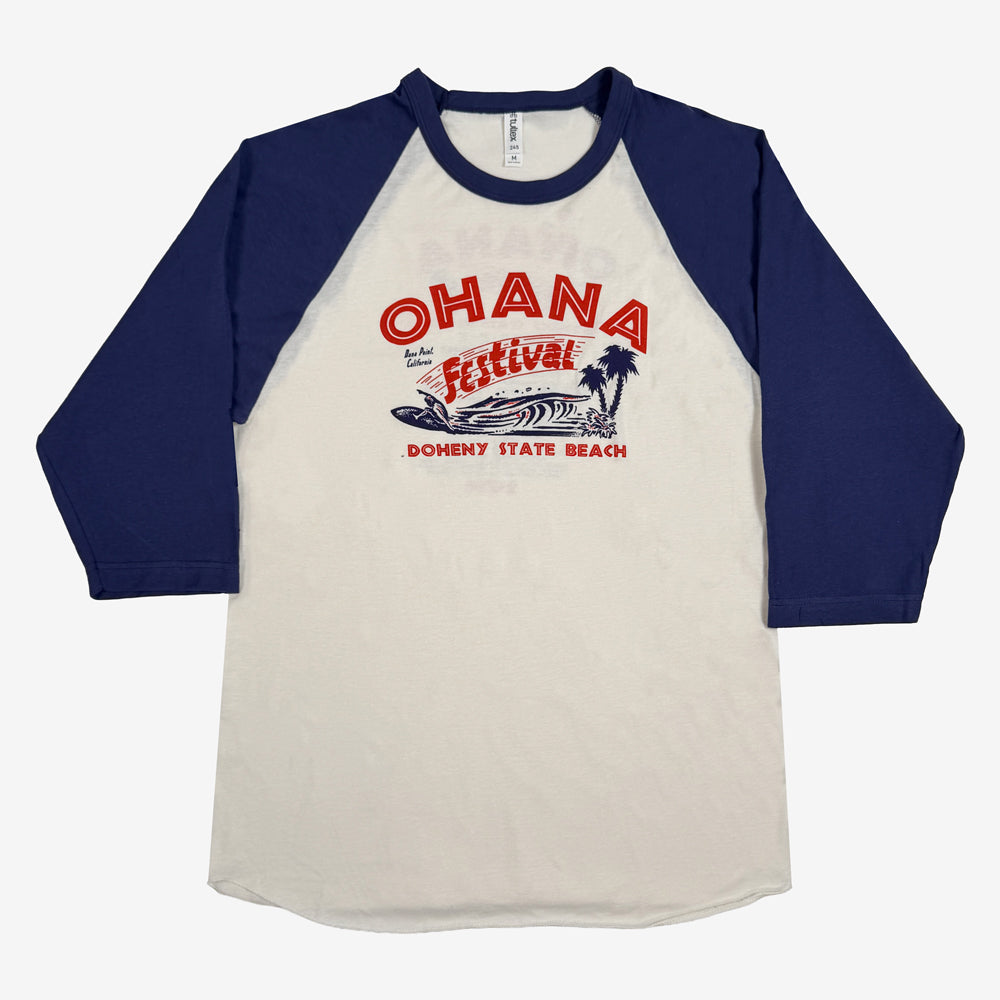 Natural Ohana Surf Meet Tee with blue raglan sleeves and red-and-blue lettering, surfer, wave, and palm artwork.