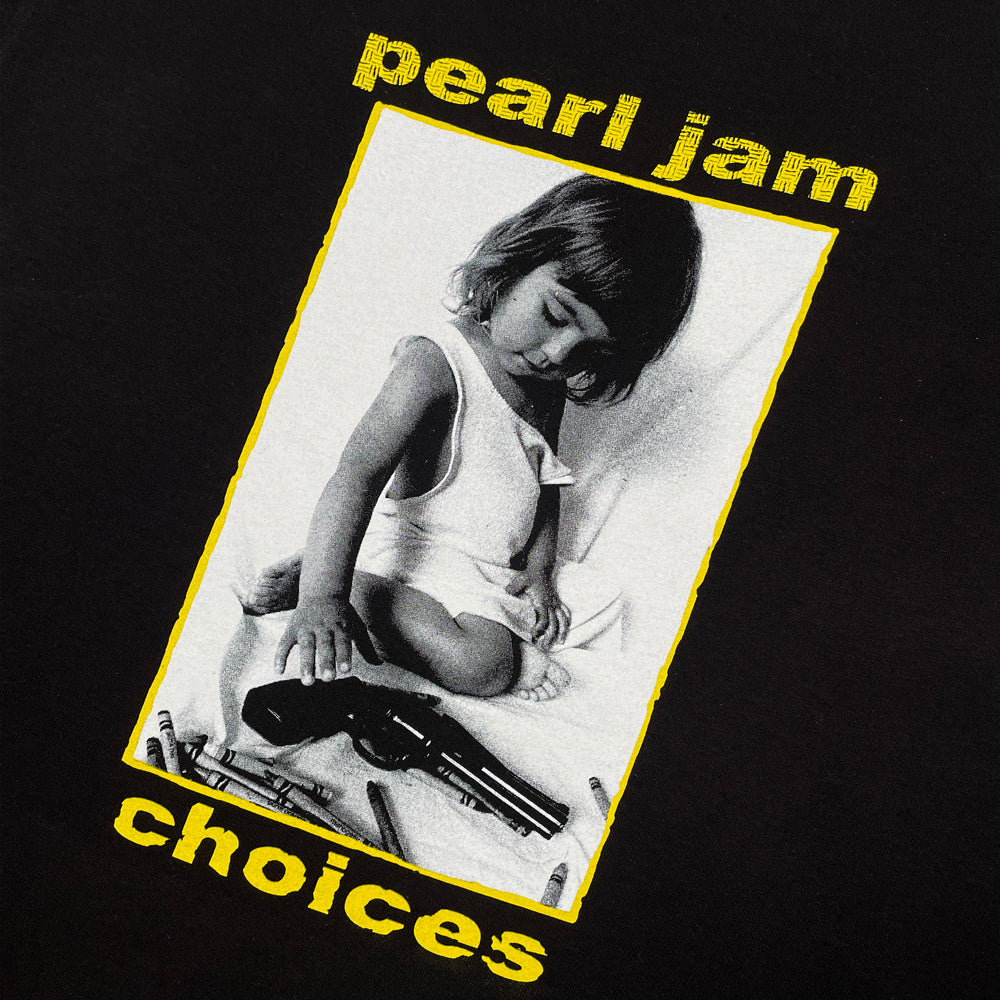 Close up of a black Pearl Jam t-shirt with graphic of a child viewing both crayons and a gun. Lettering reads "Pearl Jam Choices"