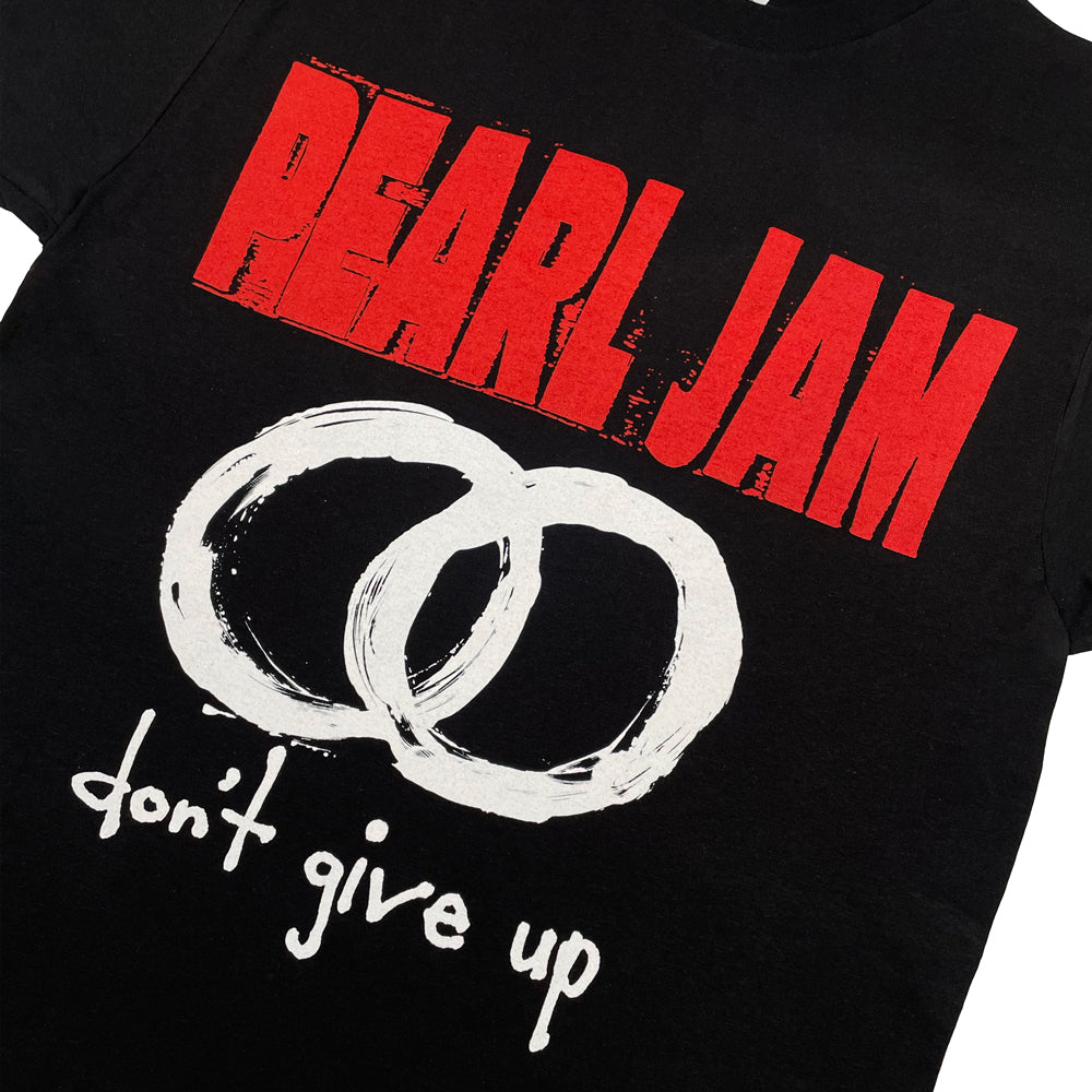 Close up of a black t-shirt with red "Pearl Jam" logo and graphic of two circles with the words "don't give up"