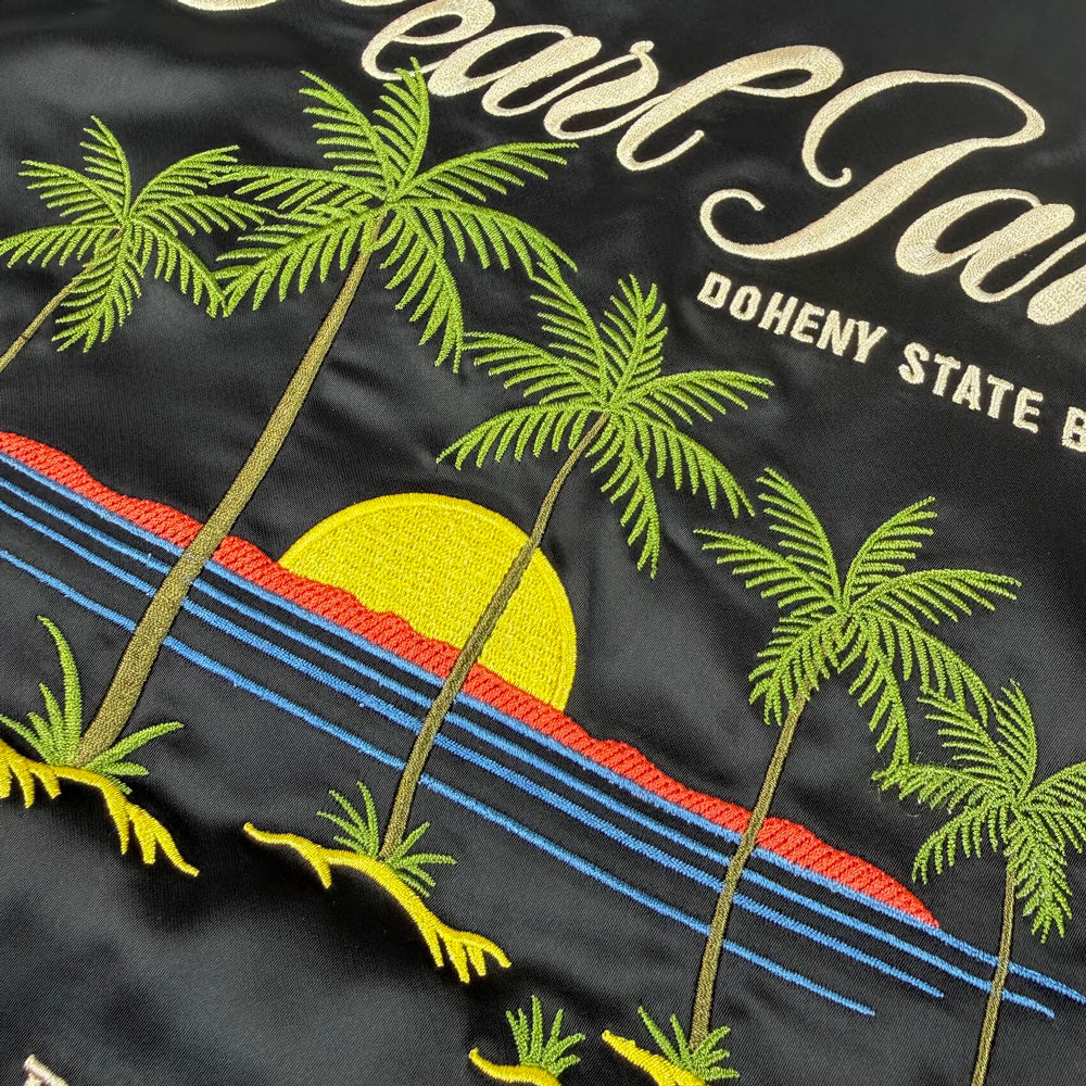 Close-up of embroidered Pearl Jam palm trees, ocean, and sunset artwork on black satin jacket

