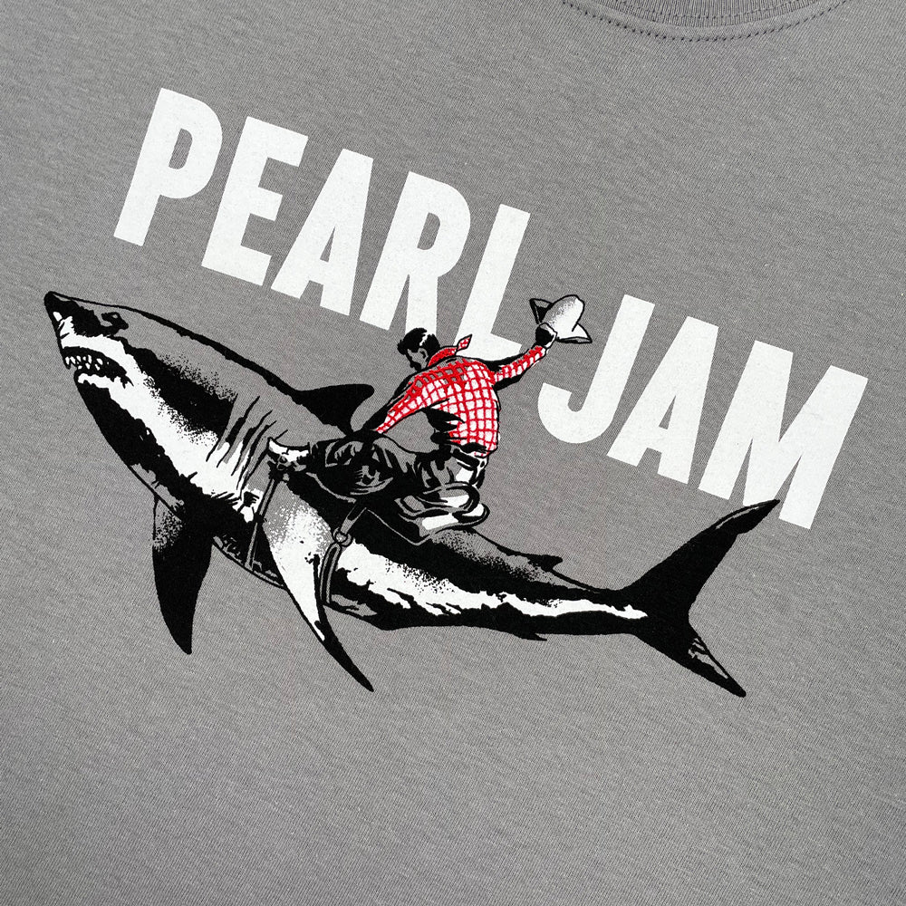 Close up of a silver Pearl Jam tee with logo reading "Pearl Jam" above a graphic of a cowboy riding a shark