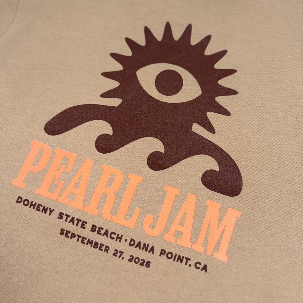 Close-up of brown Wave Lord character and orange Pearl Jam Dana Point graphic on sandstone crewneck