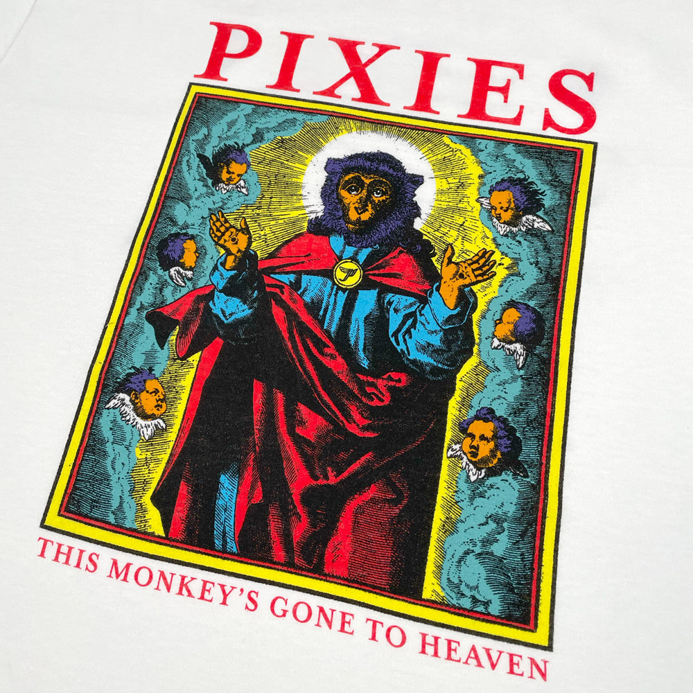A close up of a white t shirt against a white background with red text reading "Pixies." Below the text is a design of a monkey dressed like a saint surrounded by cherubs and clouds. Below this design there is red text reading "This Monkey's Gone to Heaven"