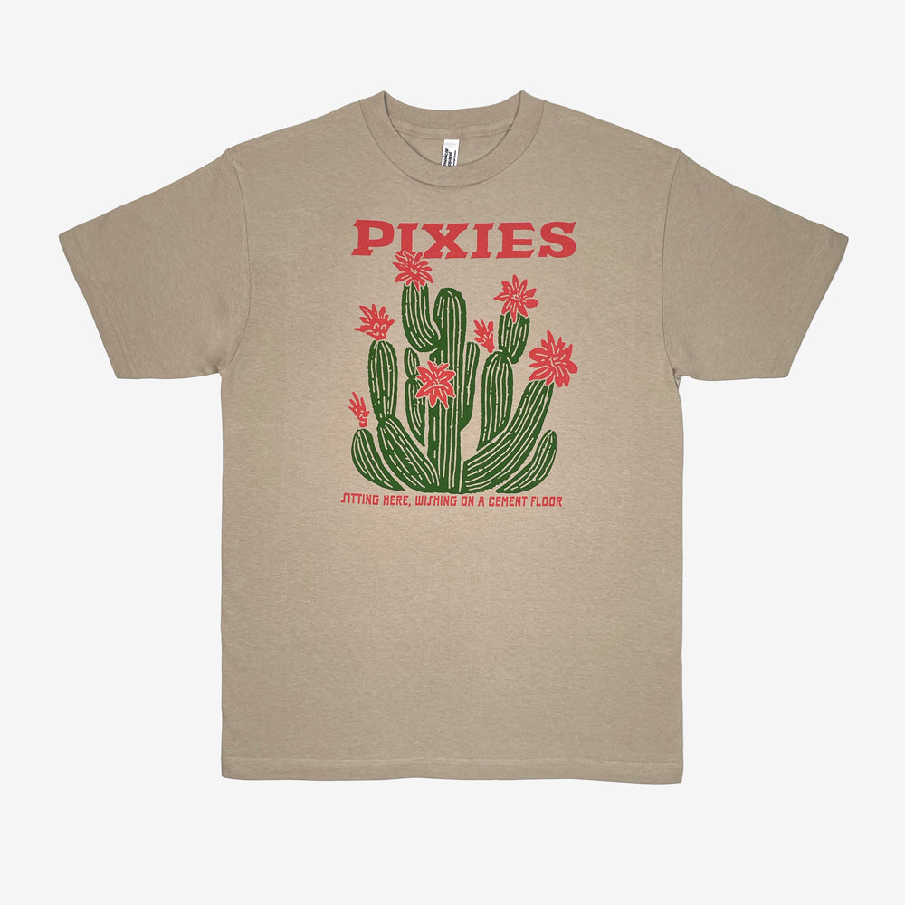 A sand t-shirt featuring a graphic of green cacti with light red flowers and the word 'PIXIES' printed in light red above them and light red text reading "Sitting here, wishing on a cement floor" below. Displayed on a white background.