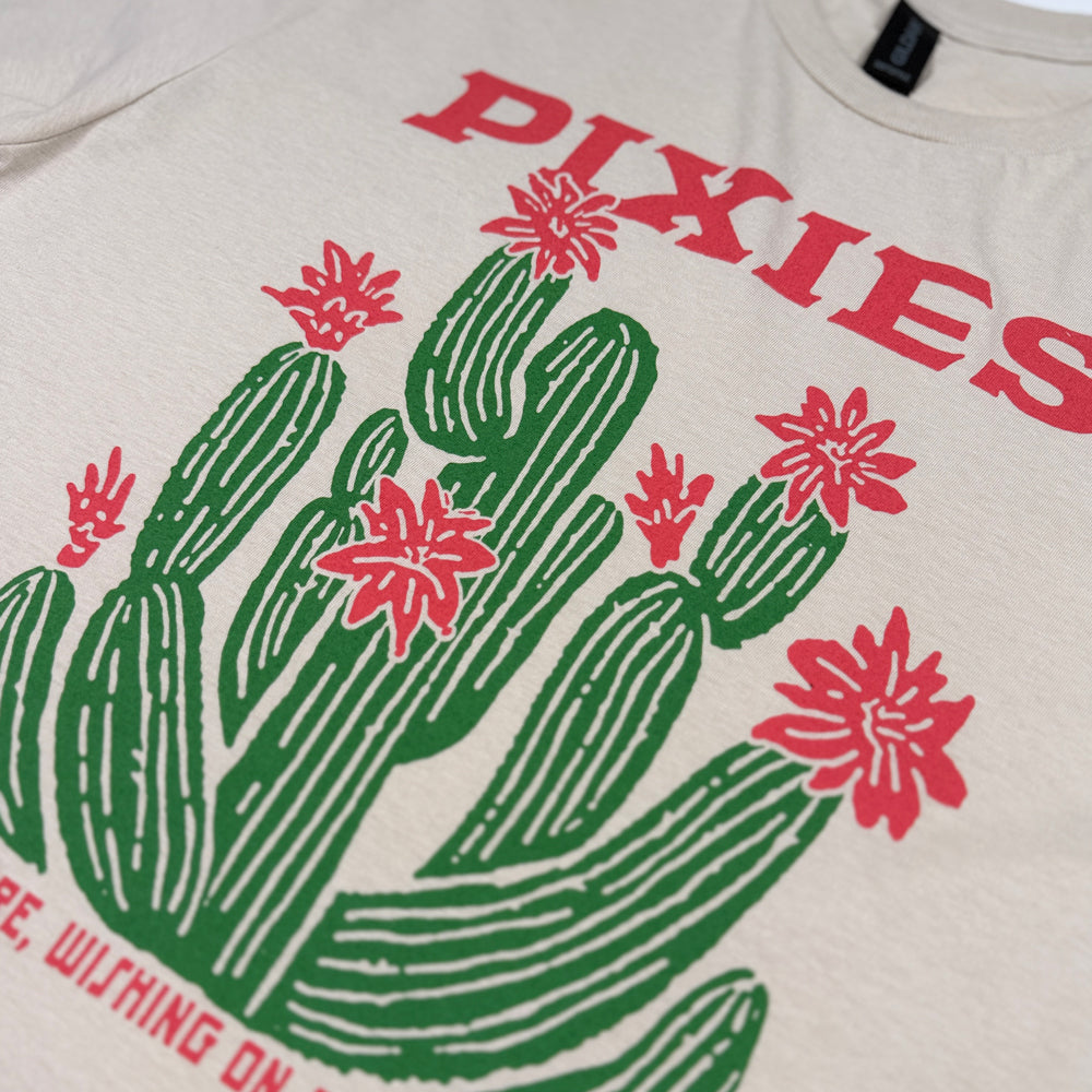 Close-up of red Pixies lettering and the green cactus with red flowers on the sand Cactus Tour Tee.
