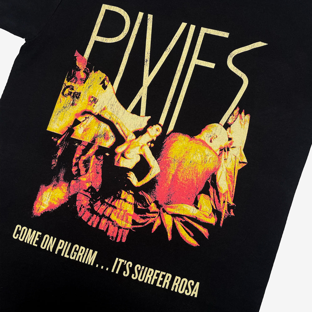 A close up of  black t shirt against a white background with faded yellow text reading "Pixies" above a yellow and light red design of a woman posing and a man with his back turned. Below the design is faded yellow text reading "Come on Pilgrim... It's Surfer Rosa"