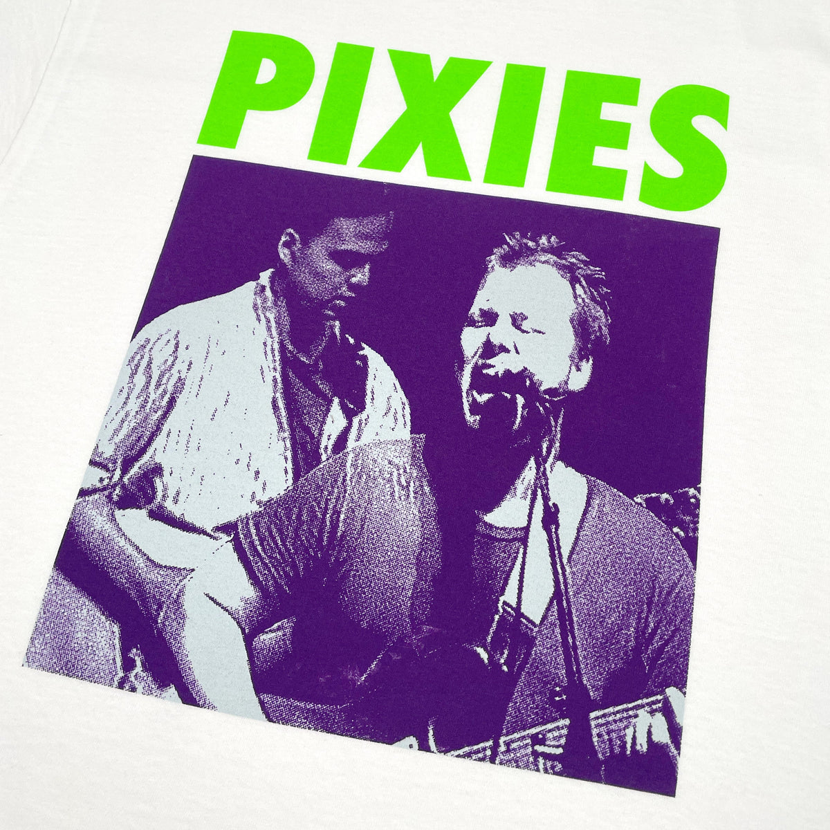 Close up of a white Pixies t-shirt with green "Pixies" Logo and a purple photo of band performing
