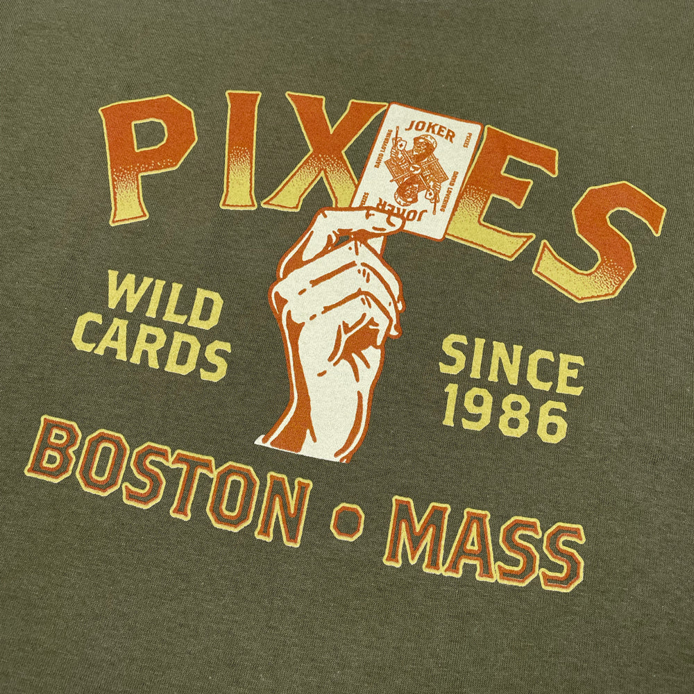 Military green shirt against a white background with yellow and orange text reading "Pixies Wild Cards Since 1986 Boston Mass" with a design of a hand holding a joker playing card.