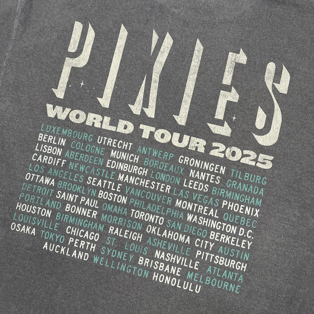 A close up of the back of a washed black tee shirt with off white text reading "Pixies world tour 2025" followed by alternating teal and off white text listing all tour locations.