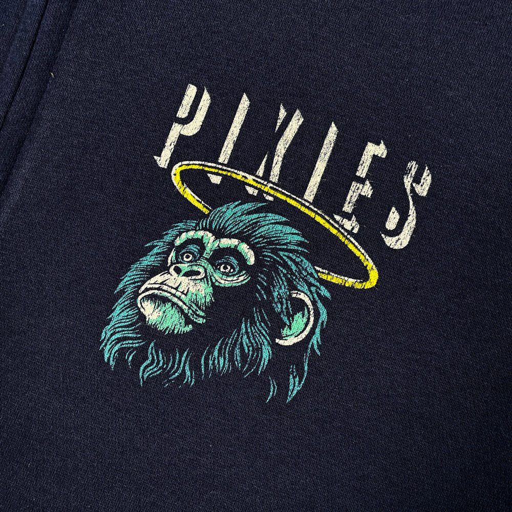 A close up of a navy zippered hoodie with light grey text reading "Pixies" on the chest with a design of a monkey with a halo below the text.