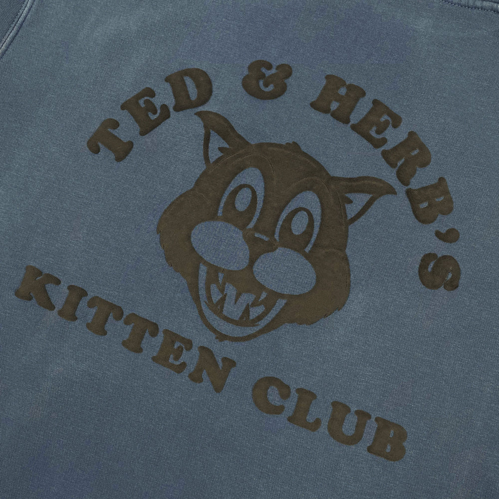 Close up of a blue pullover with black cat graphic and text reading "Ted & Herb's Kitten Club"