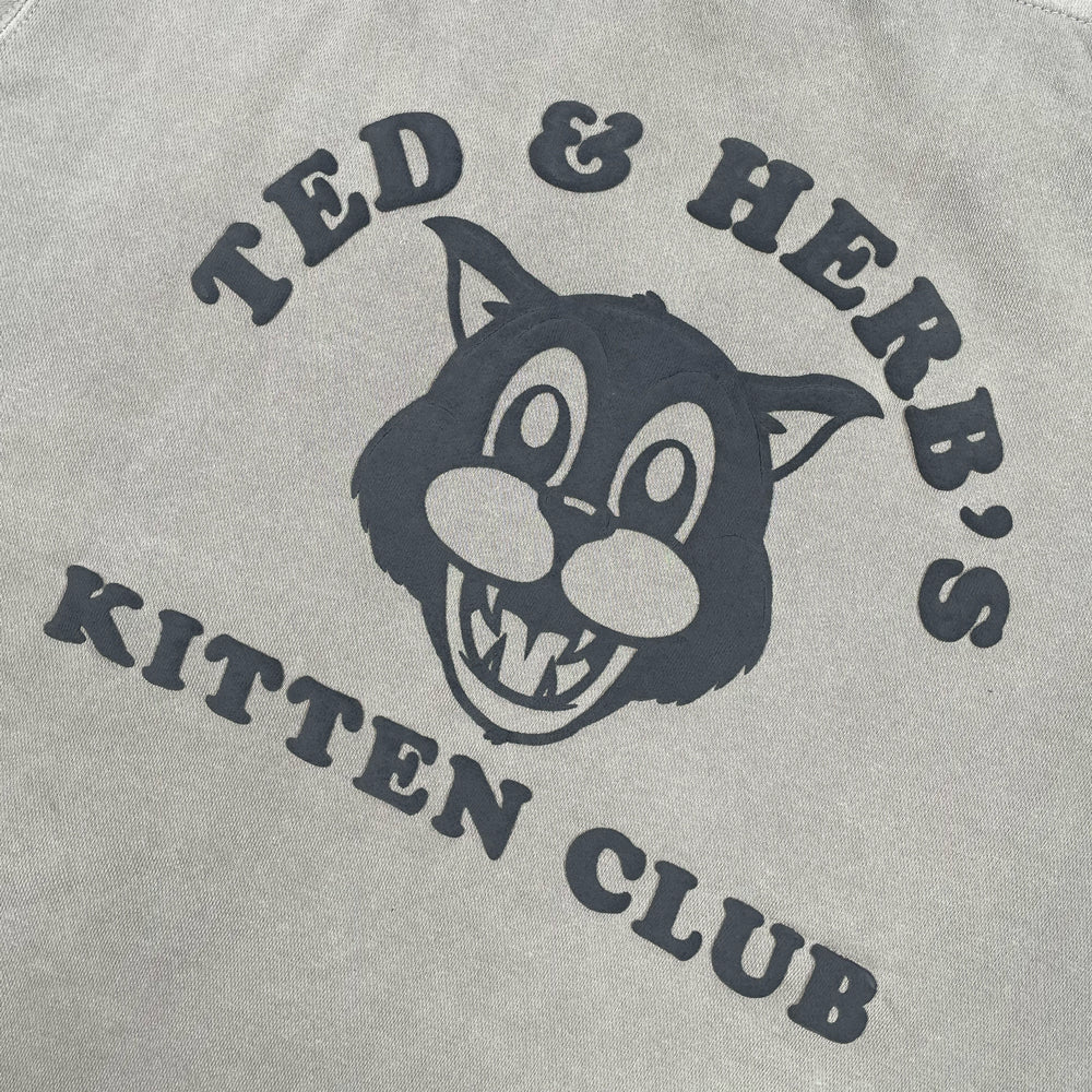 Close up of a grey pullover with Ted & Herb's Kitten Club printed and logo of a cat