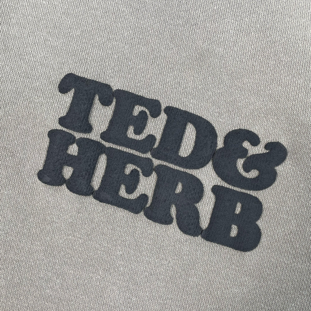Close up of a grey pullover with printed text reading "Ted & Herb" 