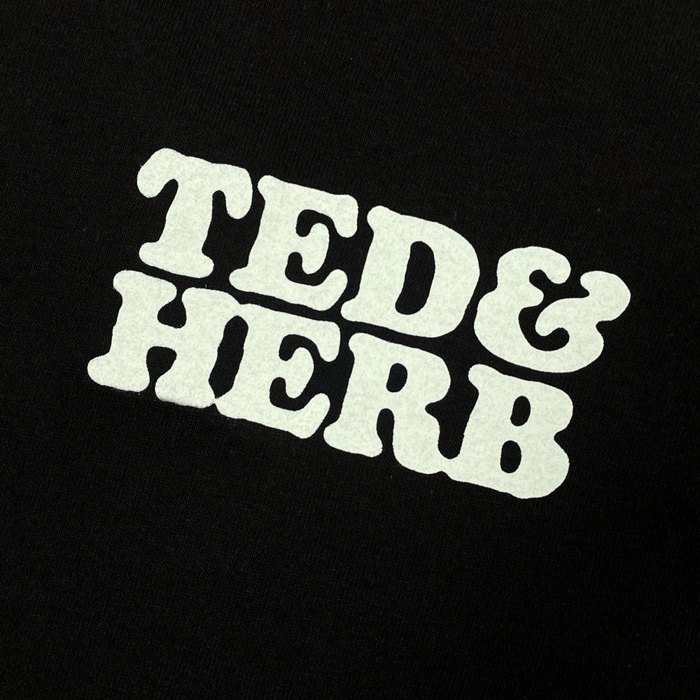 Close up of a black T shirt with white text on the chest reading "Ted & Herb"
