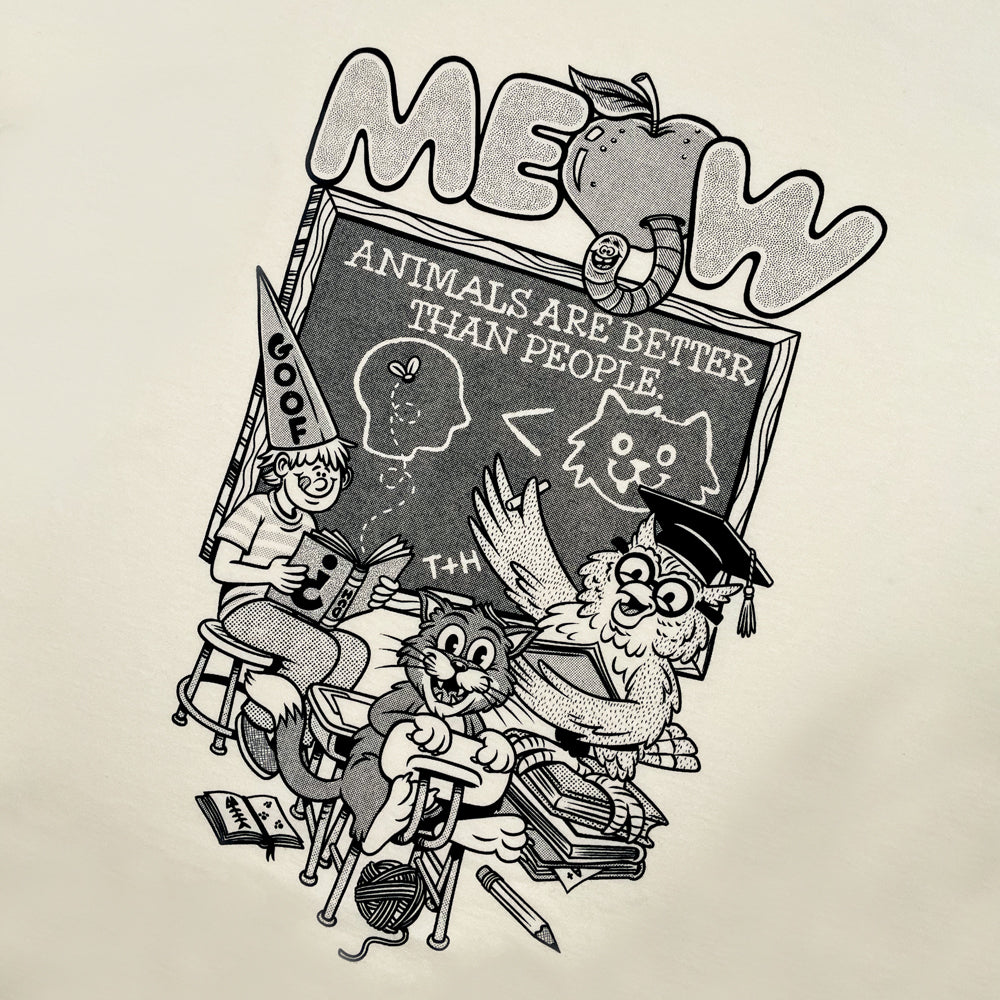 Close up of a cream T shirt with typography reading "Meow" above an image depicting a cat, a boy, and an owl in a classroom with a chalkboard reading "Animals are Better than People"